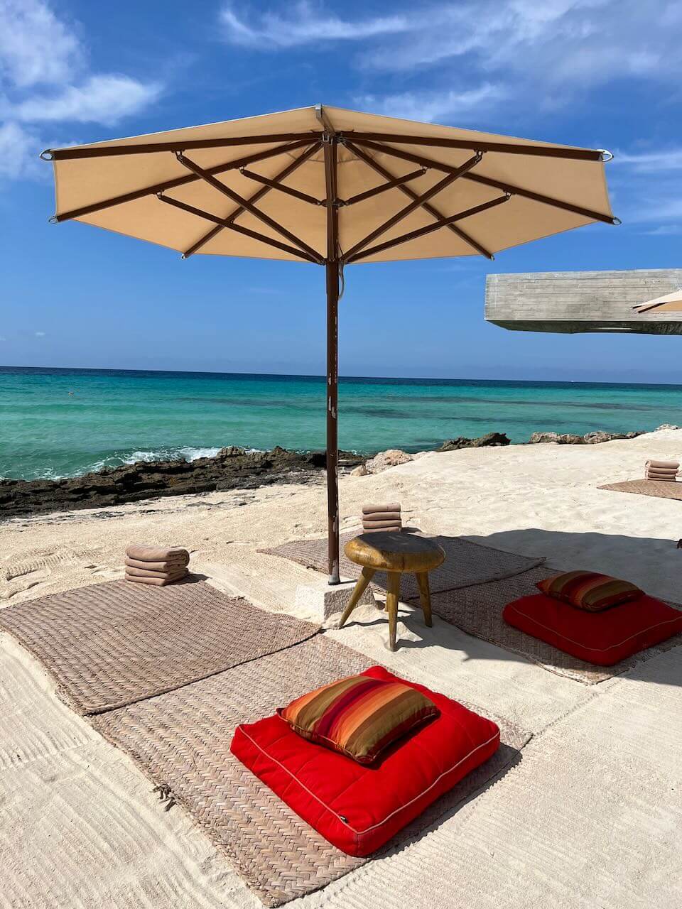 Beach with red pillows and turquoise water at La Casa de la Playa luxury hotel in Mexico.